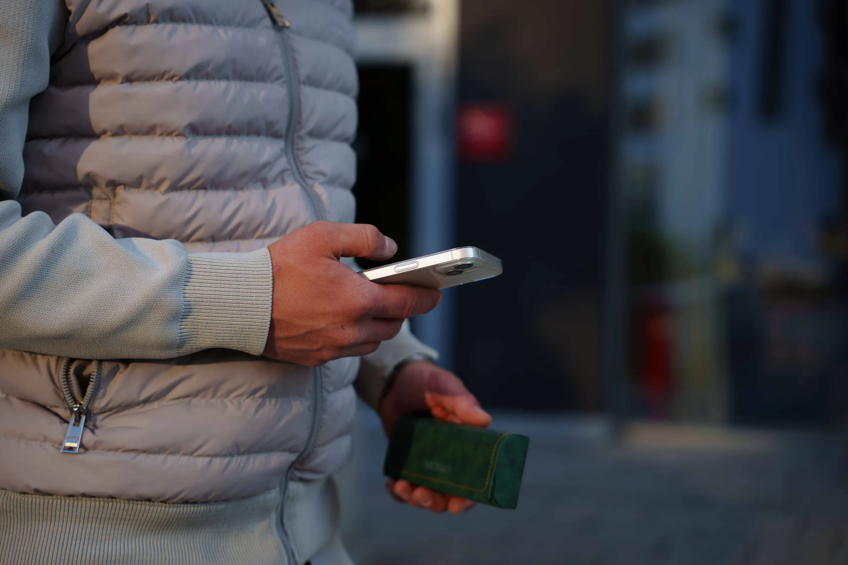 Detail — phone and a green leather wallet in hand, quilted sleeve behind