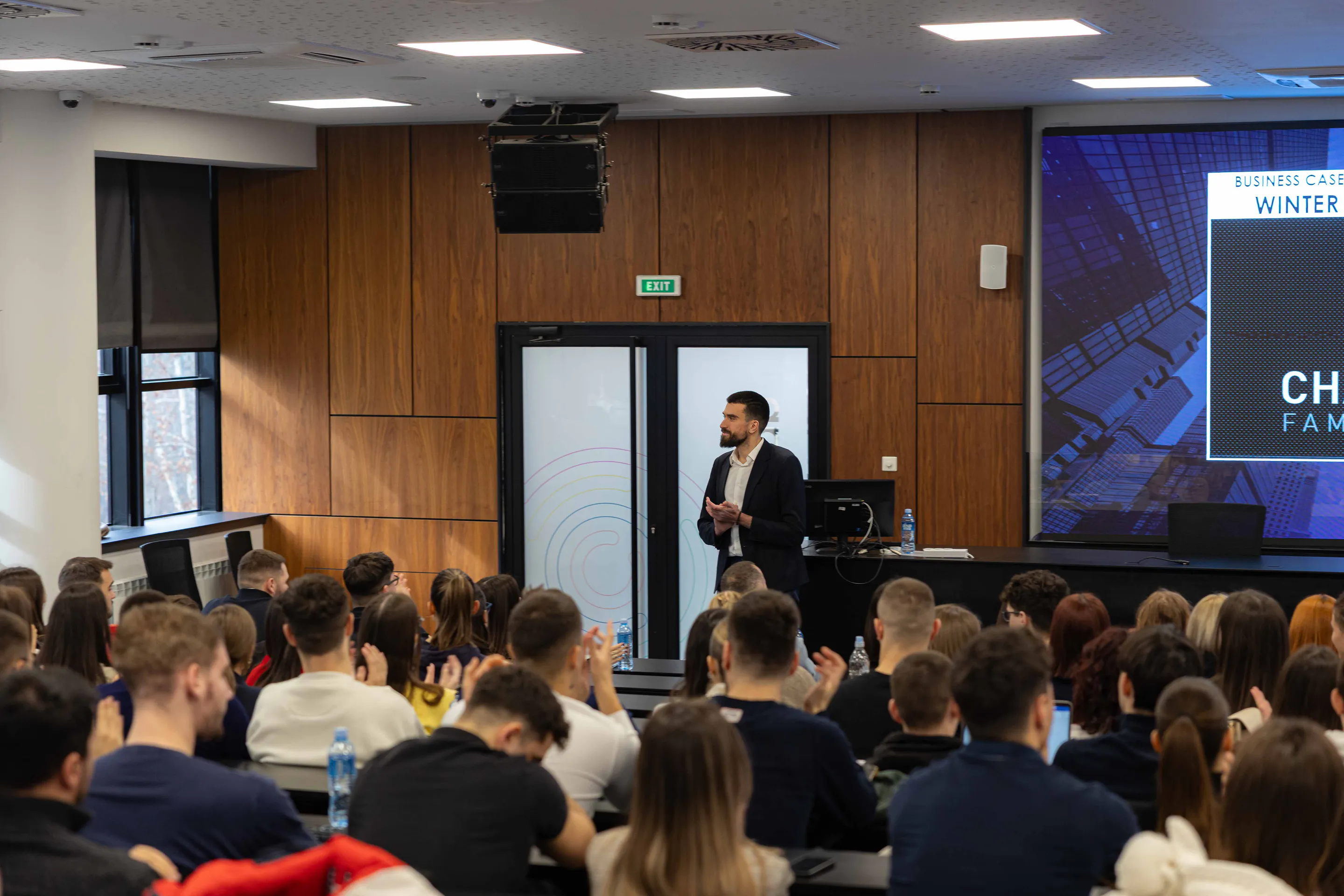 Speaker addressing the full lecture hall, the tournament screen lit behind