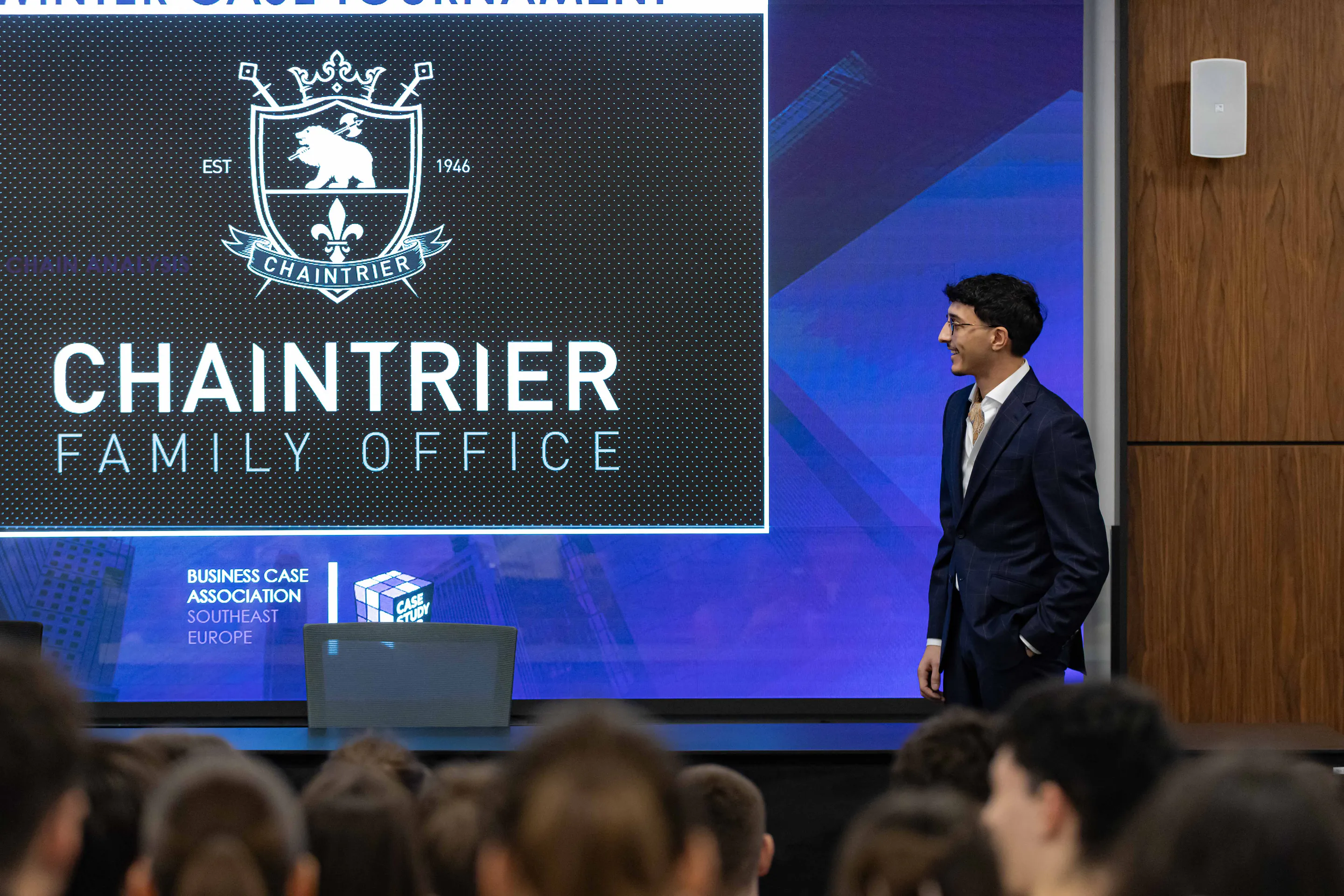 The Chaintrier Family Office crest on the hall screen as a presenter crosses the stage