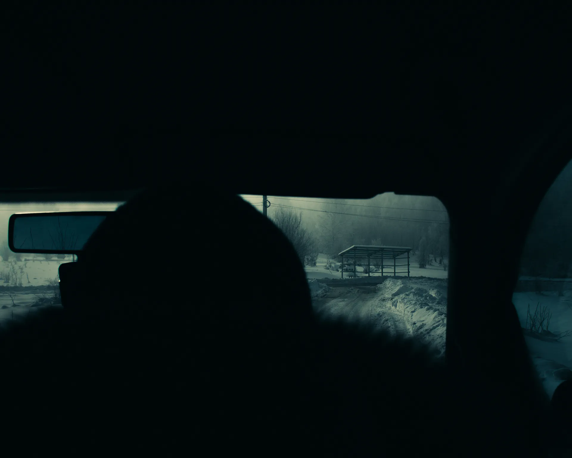 Through the rear window past a silhouetted headrest — the shelter receding