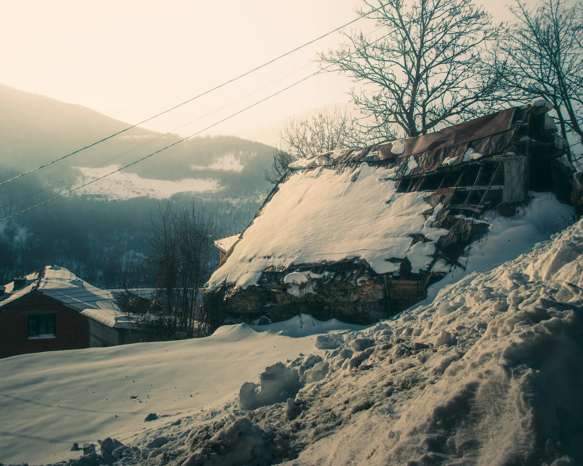 A barn roof collapsing under snow on the hillside above the village