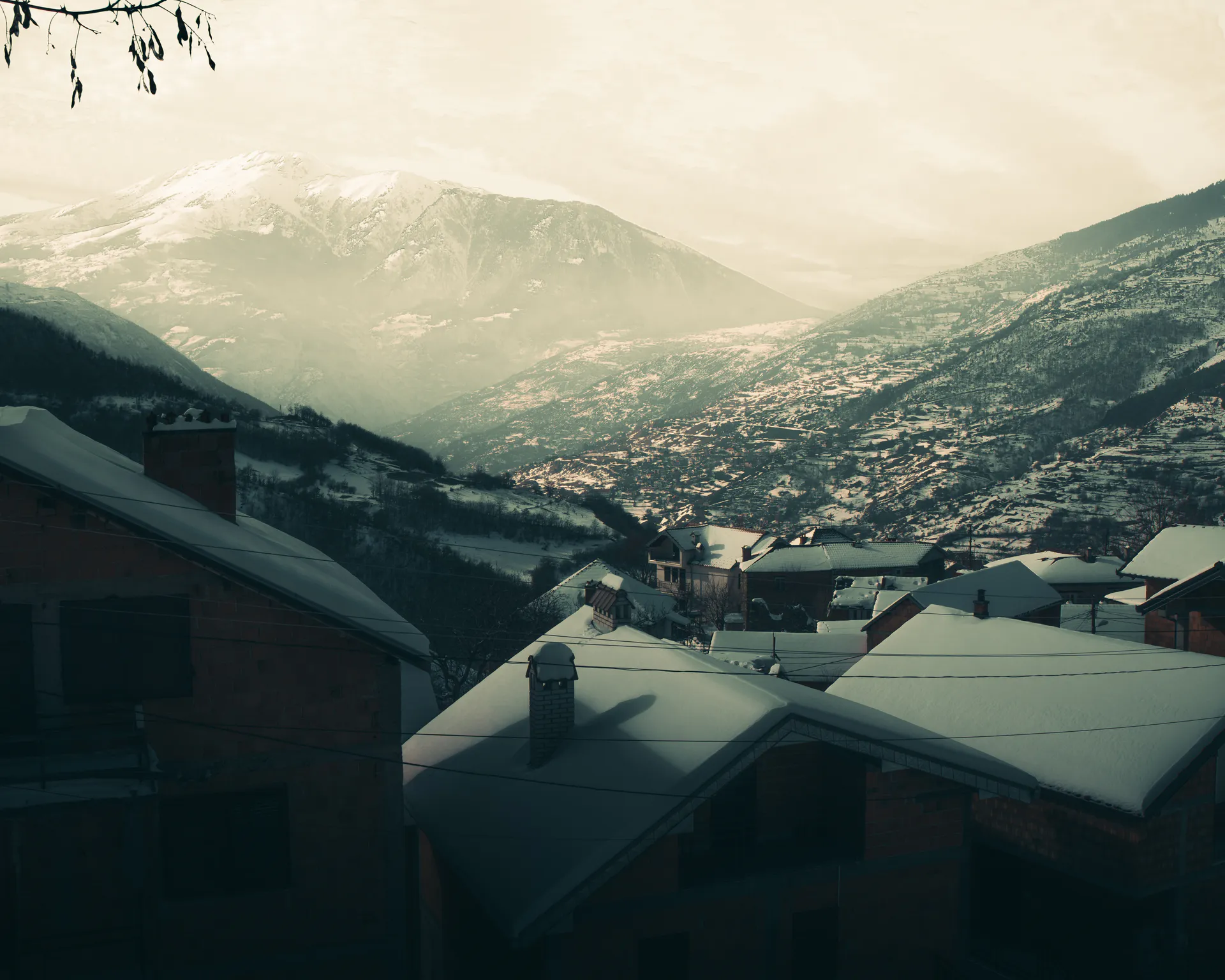 Snowed rooftops stepping down into the wide valley, a hazy mountain closing it