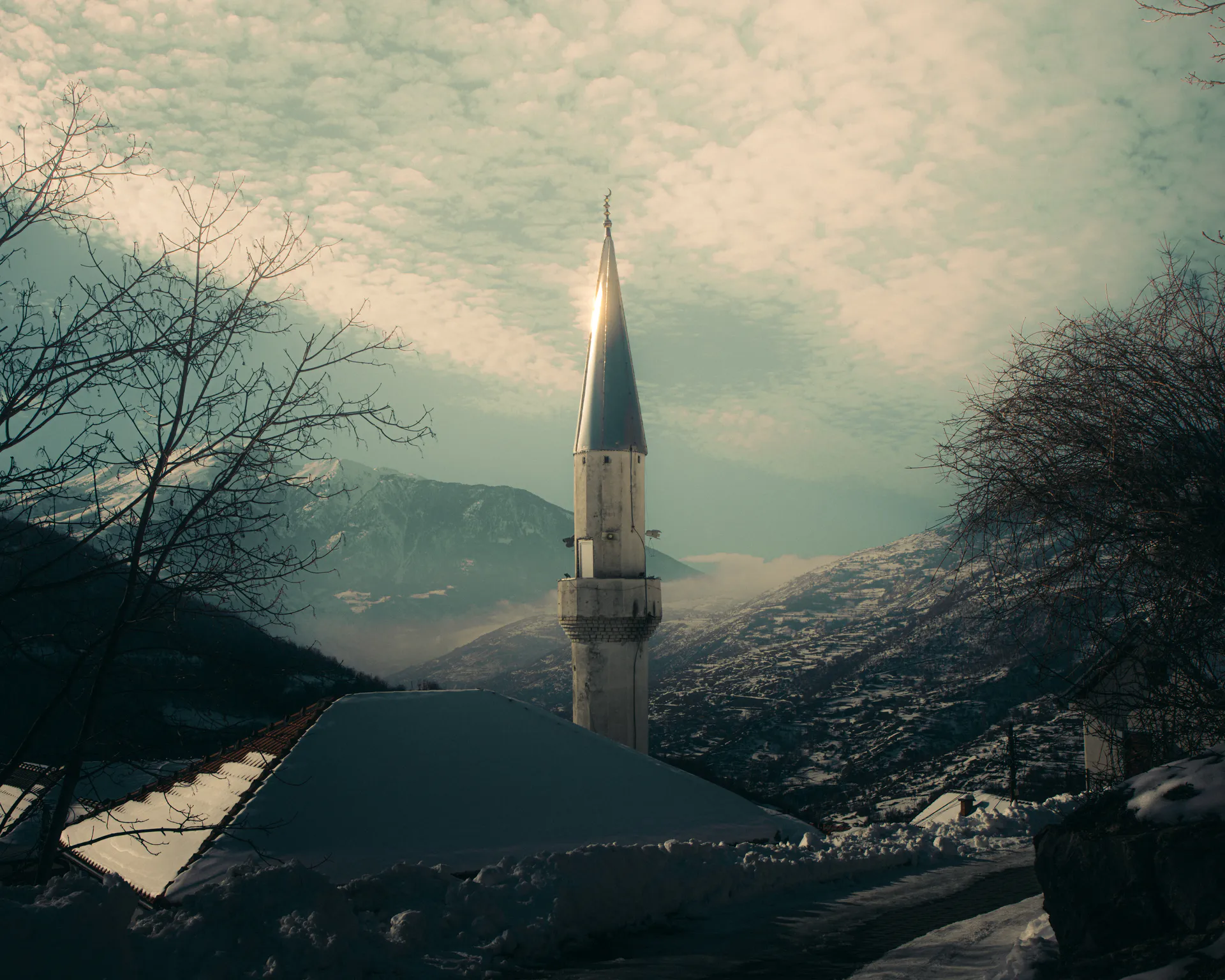 The minaret's spire glinting above snow-covered rooftops against streaked cloud