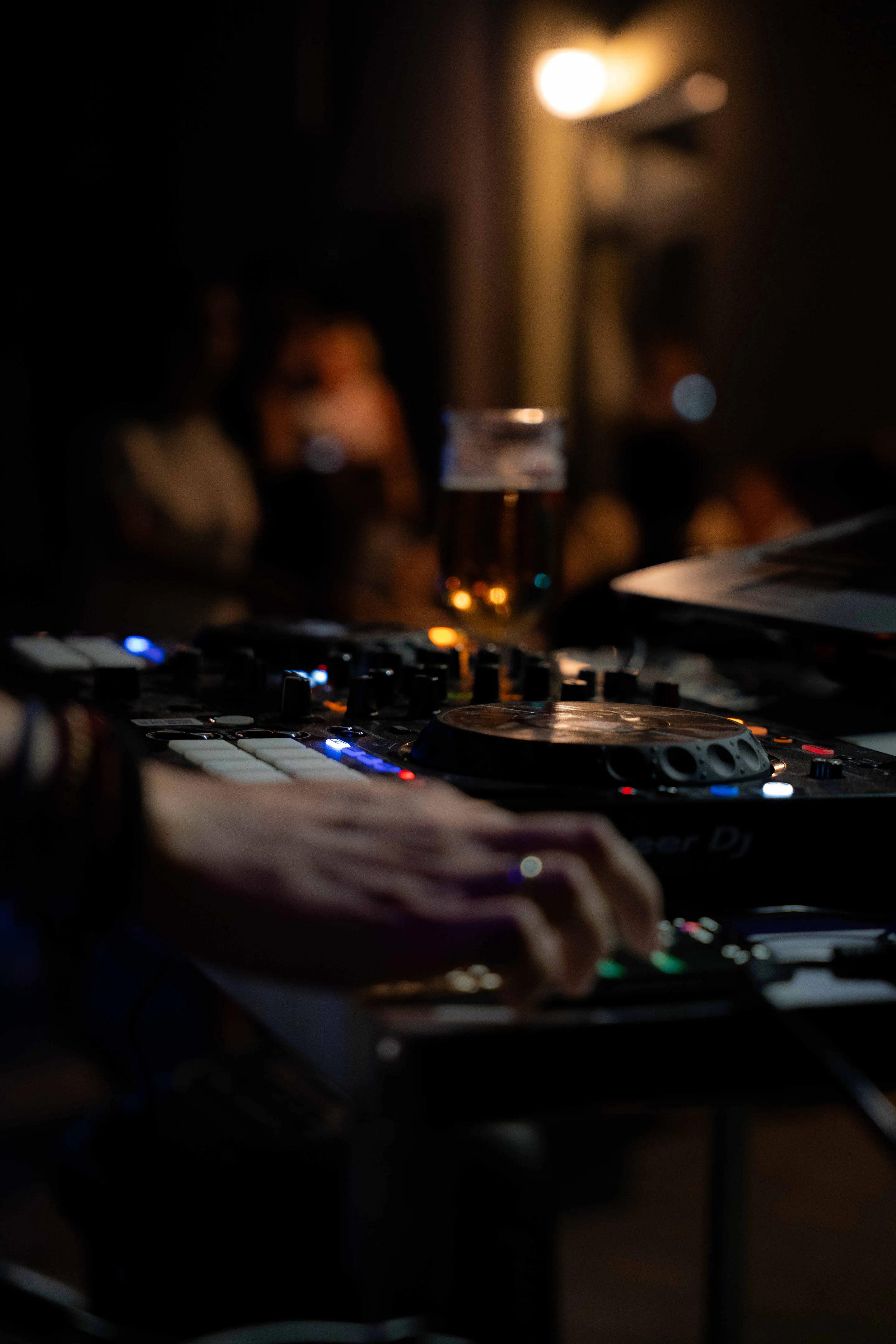 Hands on the decks, a lit pint balanced above the mixer