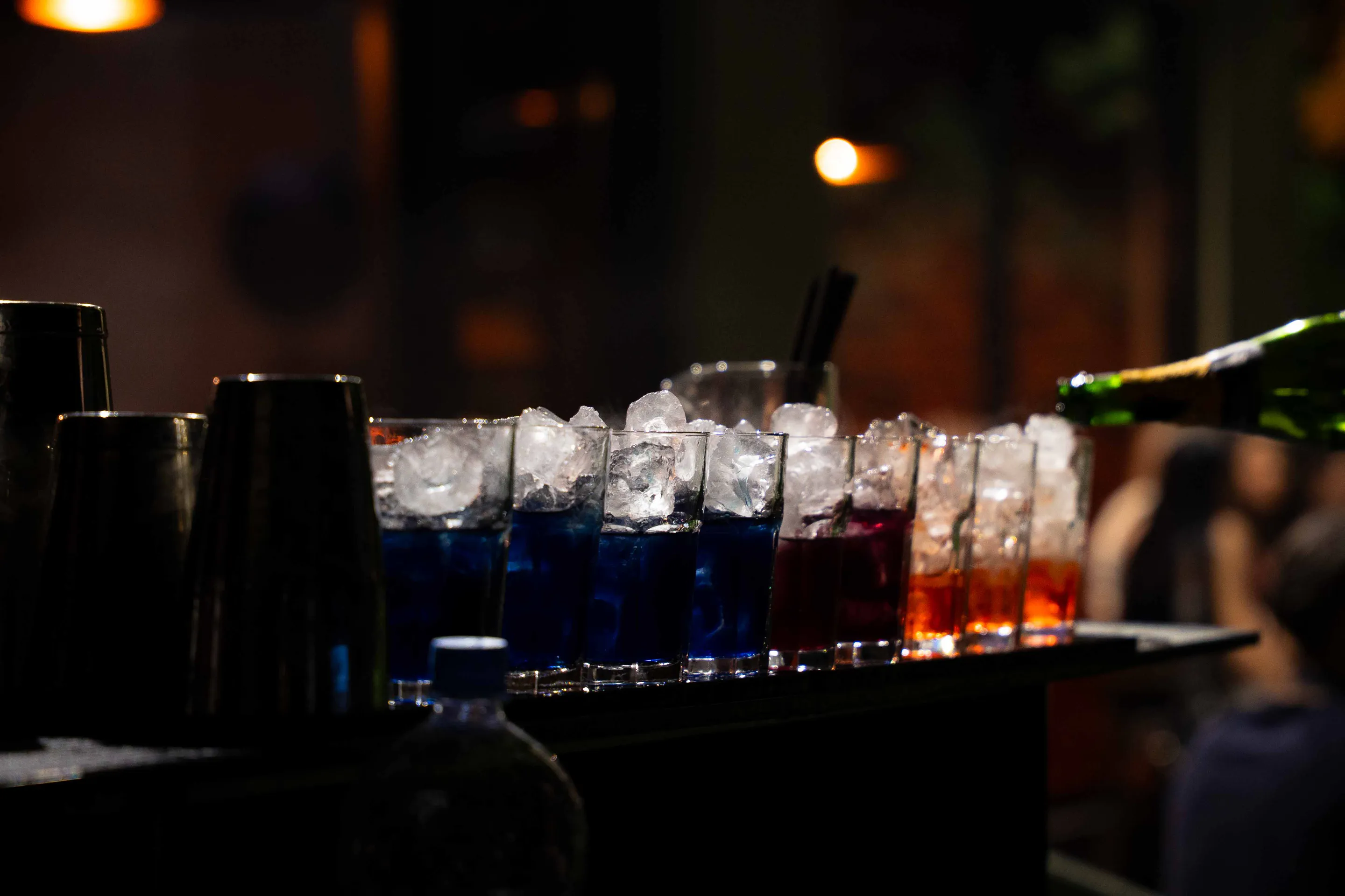 Blue and red cocktails on crushed ice as a bottle pours at the bar