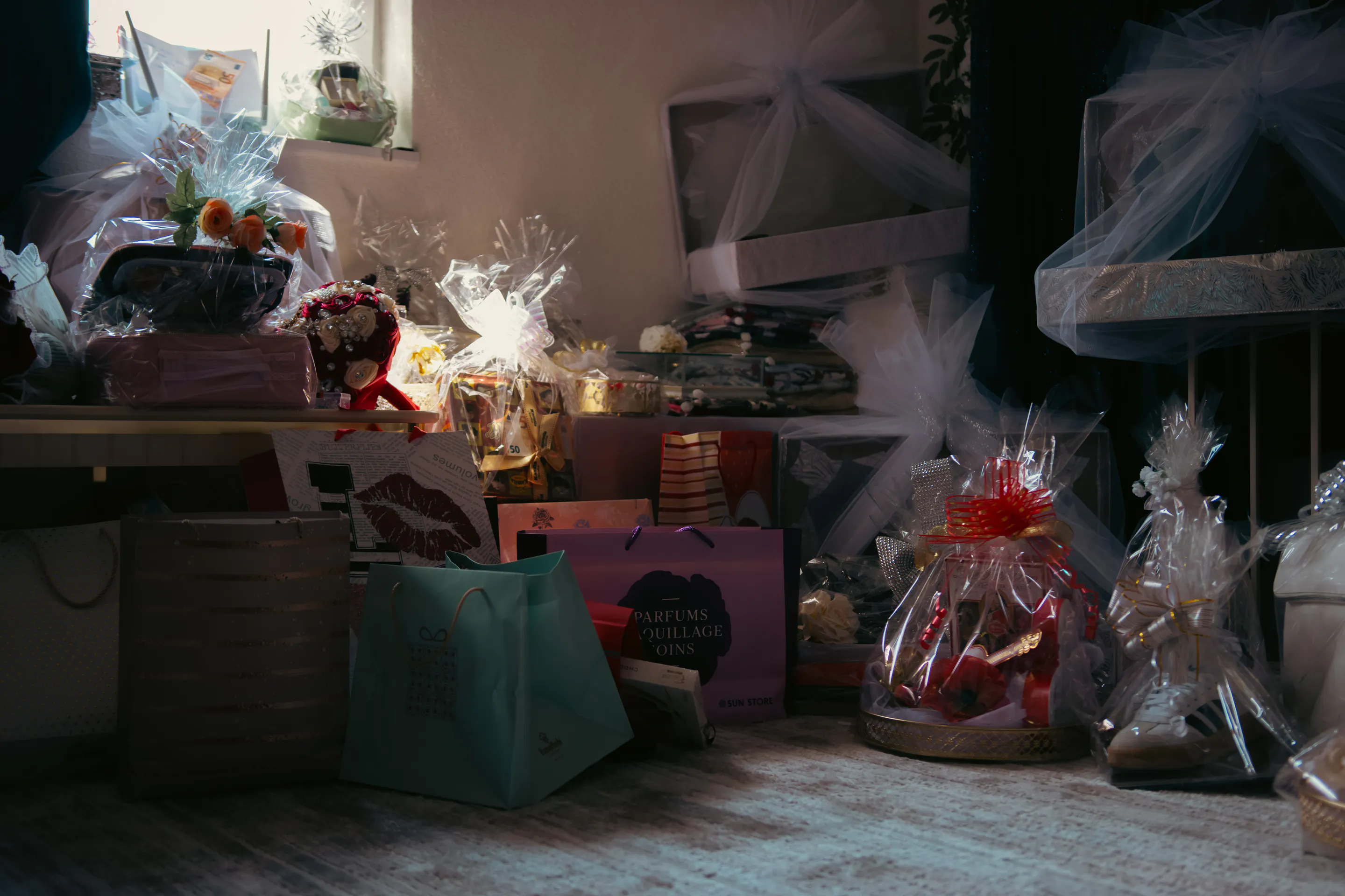 Gift bags and wrapped hampers stacked in the half-dark of the gift room