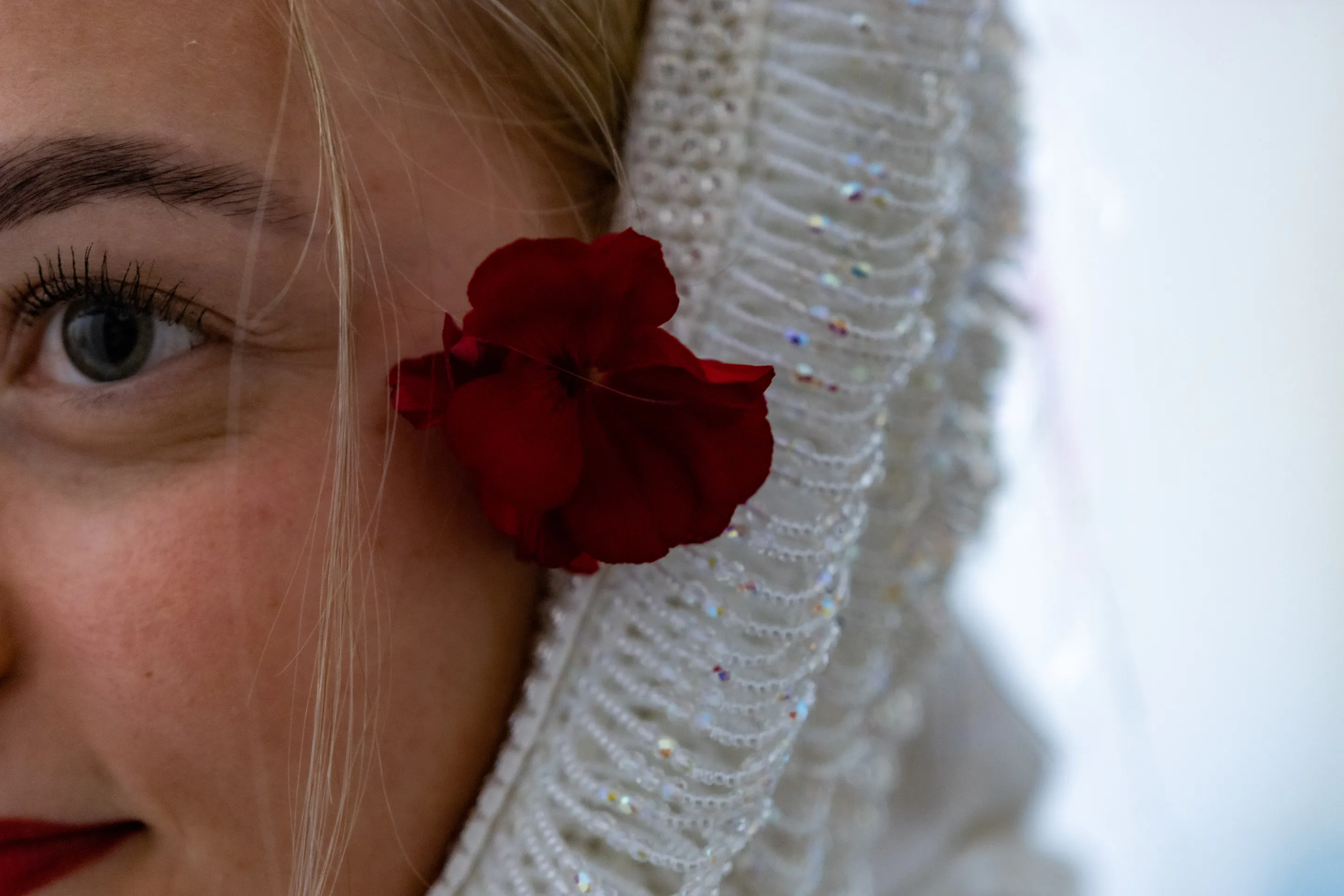 Close view of her eye beneath the beaded bonnet, a red flower fixed at its edge