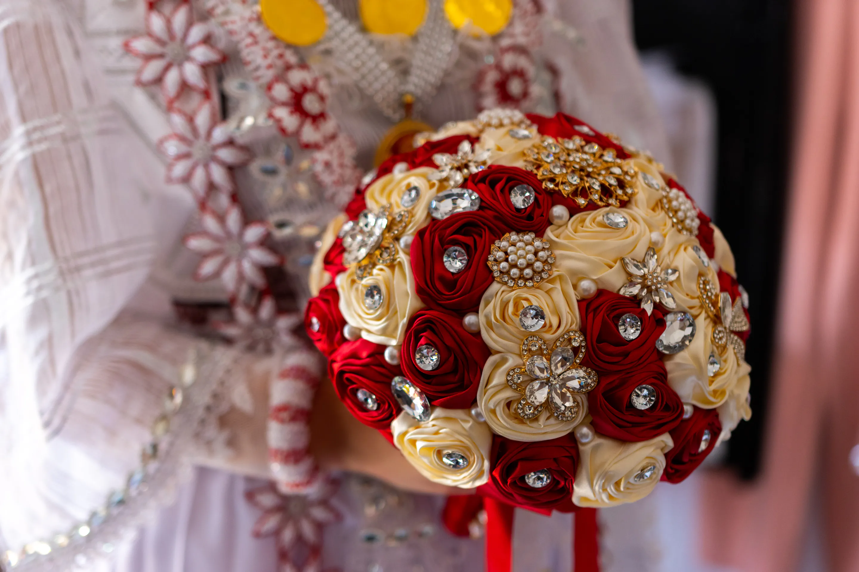 The brooch bouquet of red and gold flowers resting against the beaded sleeve