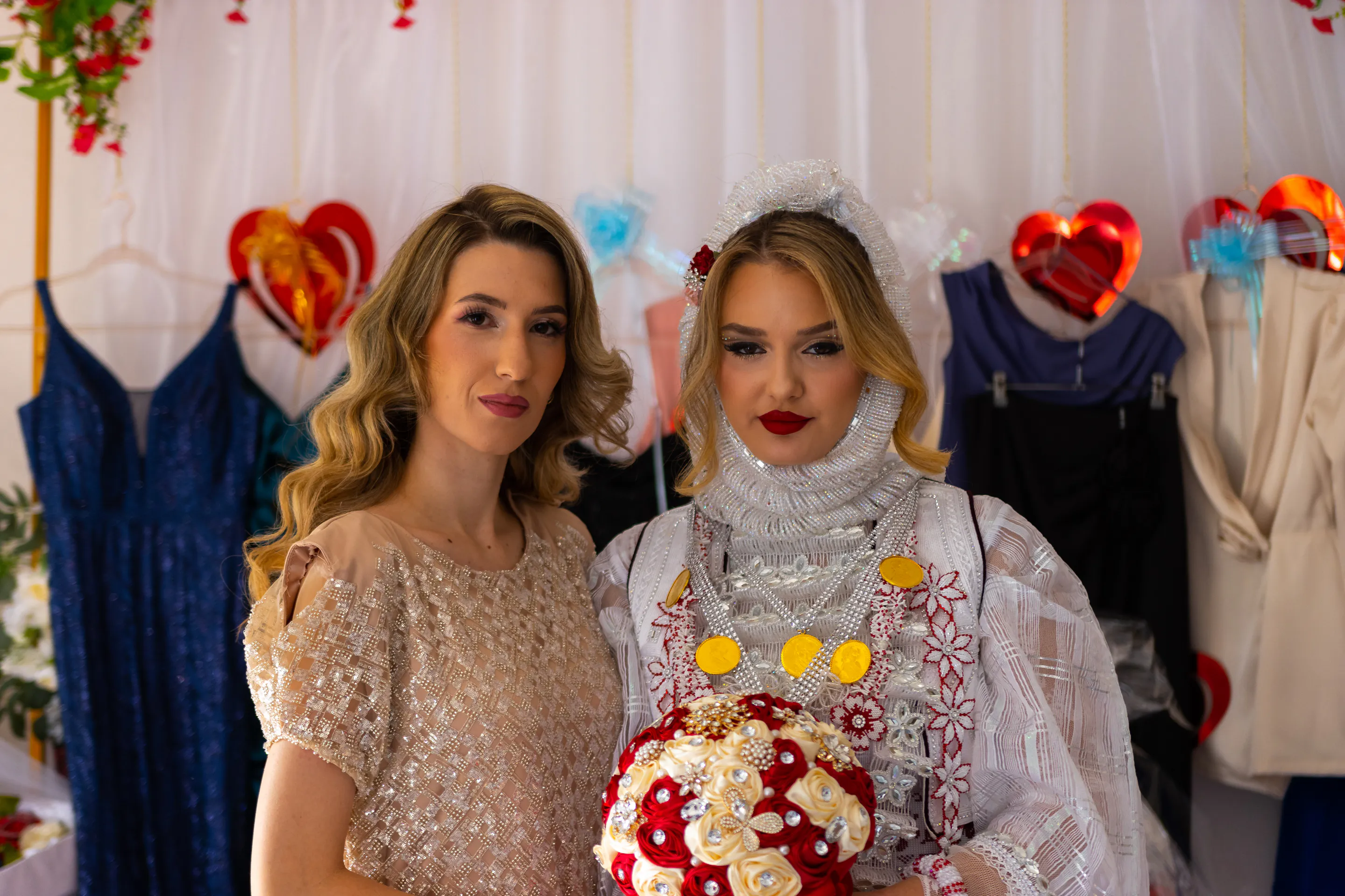 The bride-to-be and her maid of honour before a backdrop of hearts, the bouquet held between them