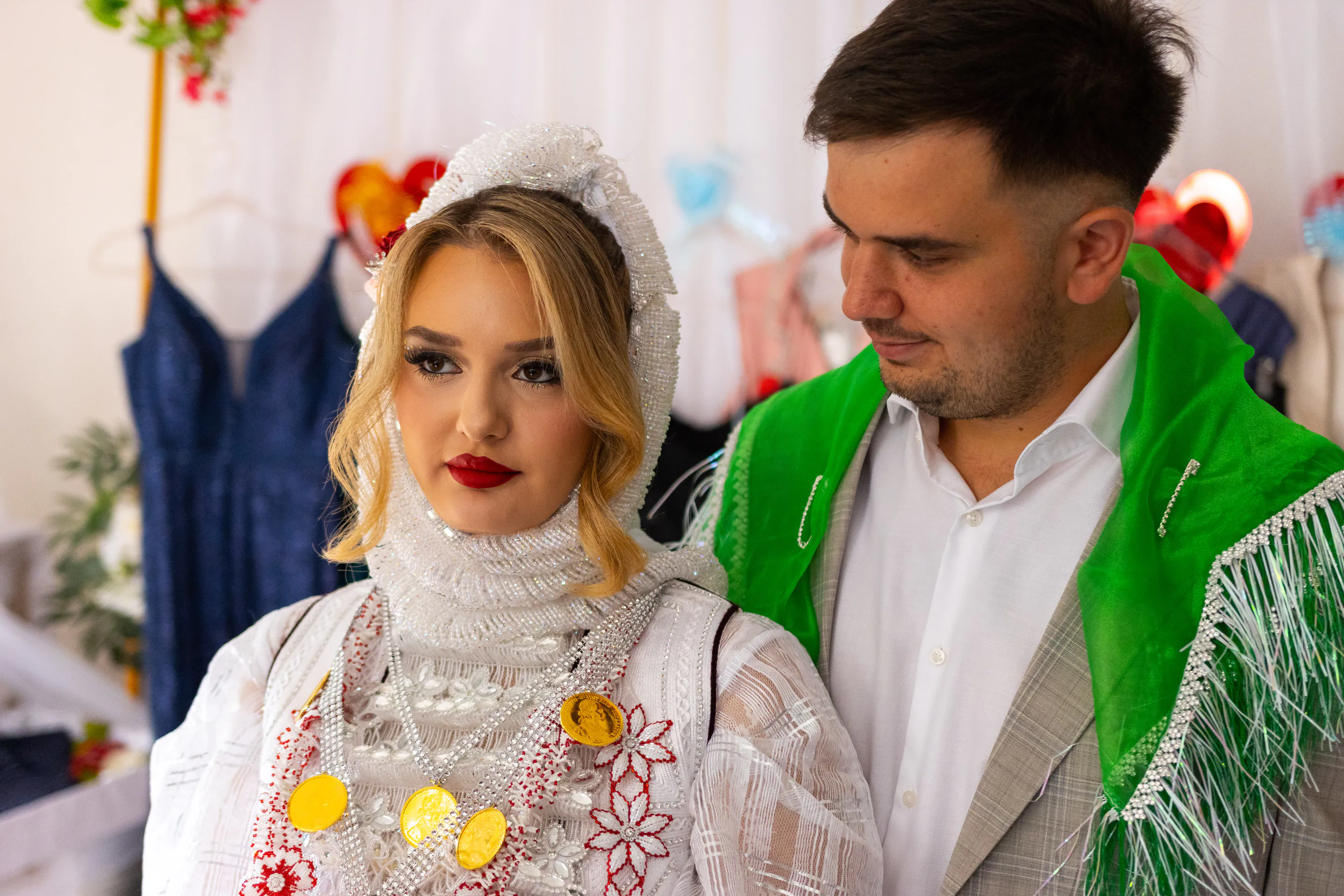 The couple side by side indoors — beaded whites against the grey suit and green shawl