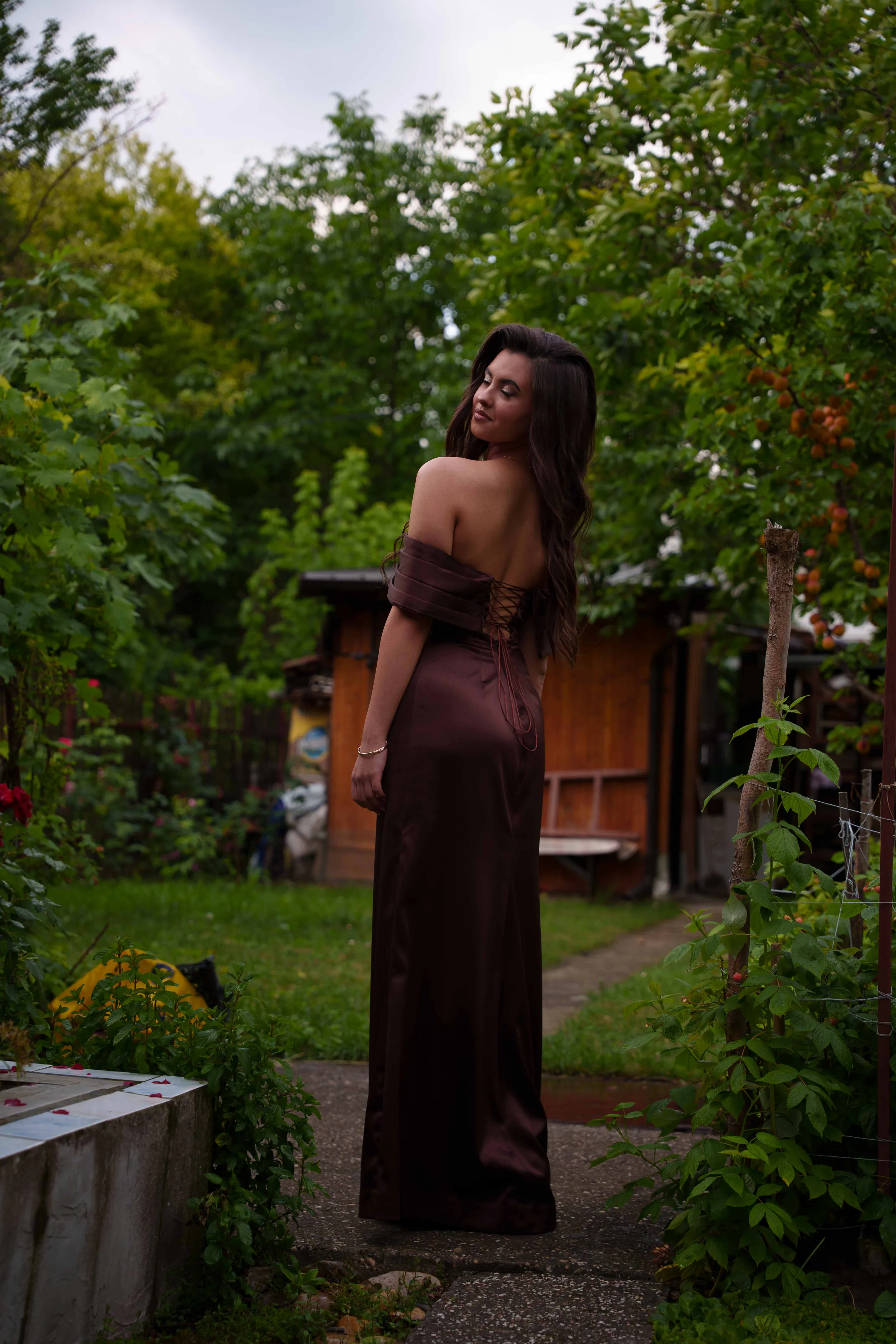 Walking the garden path away from camera, looking back over her shoulder
