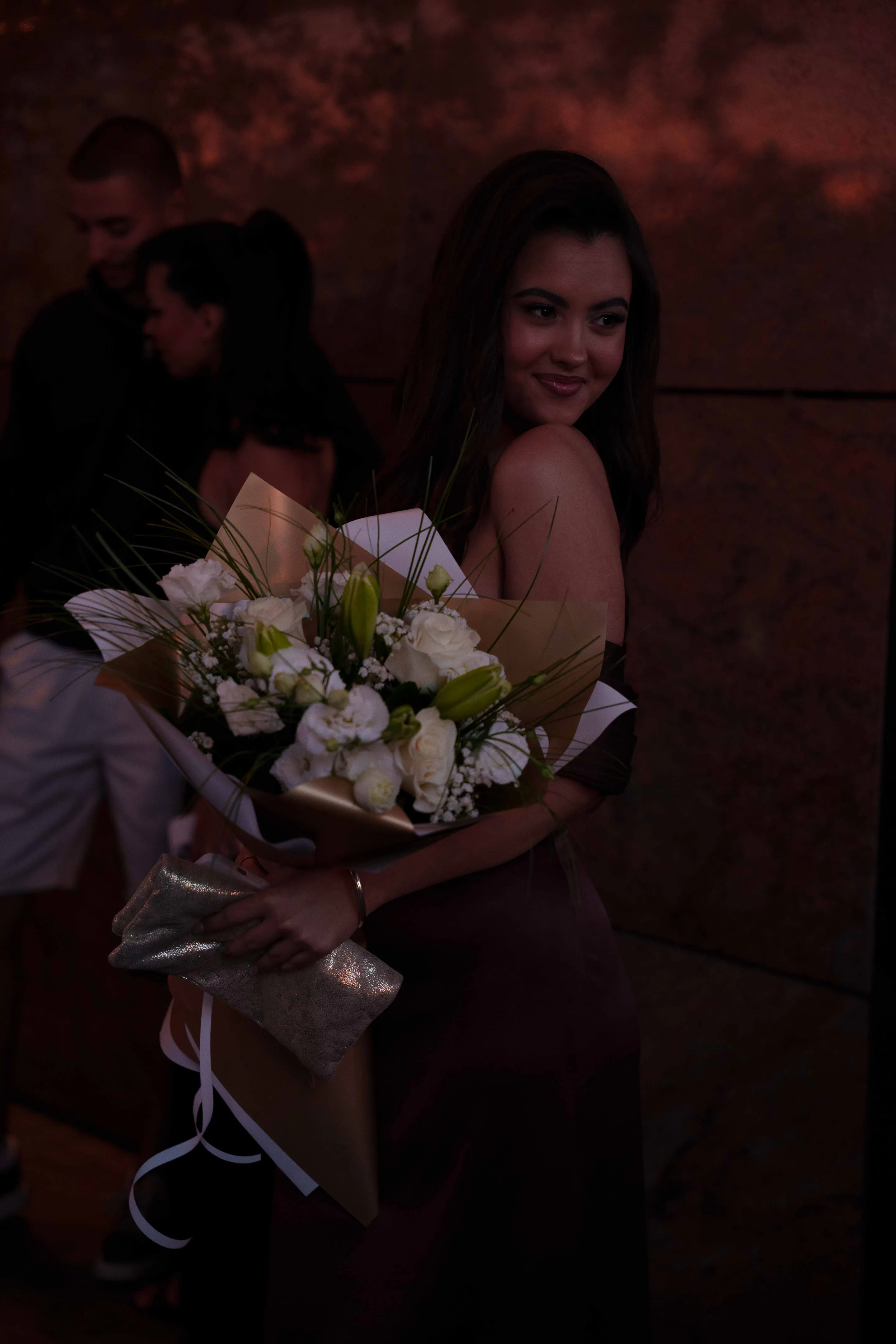 Night frame washed in red light, the white bouquet in her arms