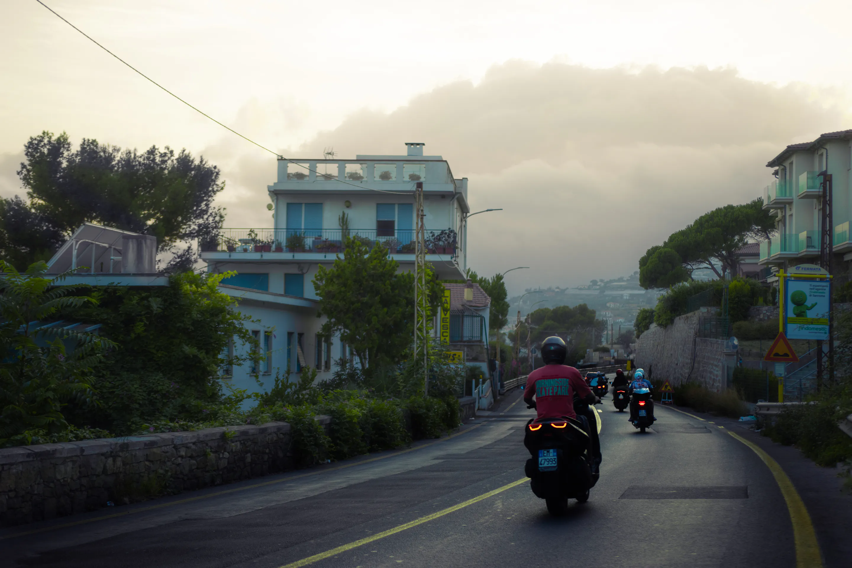 Three scooters strung down the coastal road past blue shutters