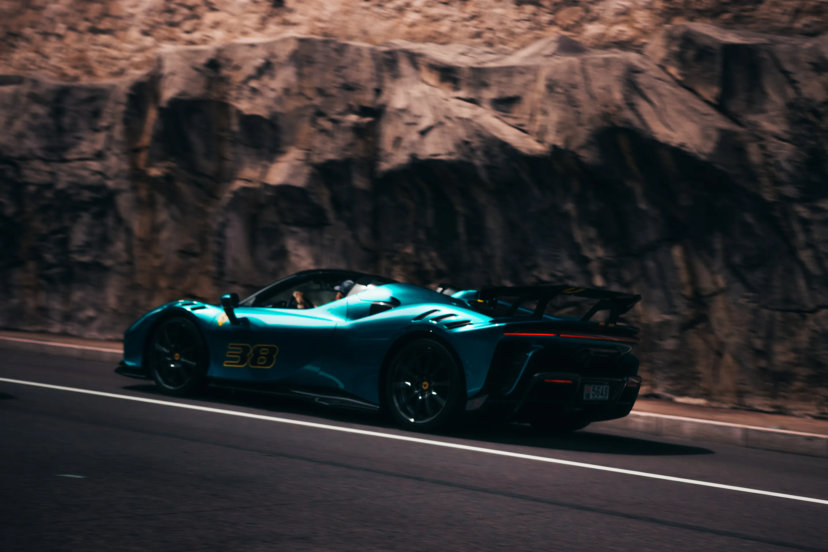 Teal roadster, number 38, panned past the sunlit cliff