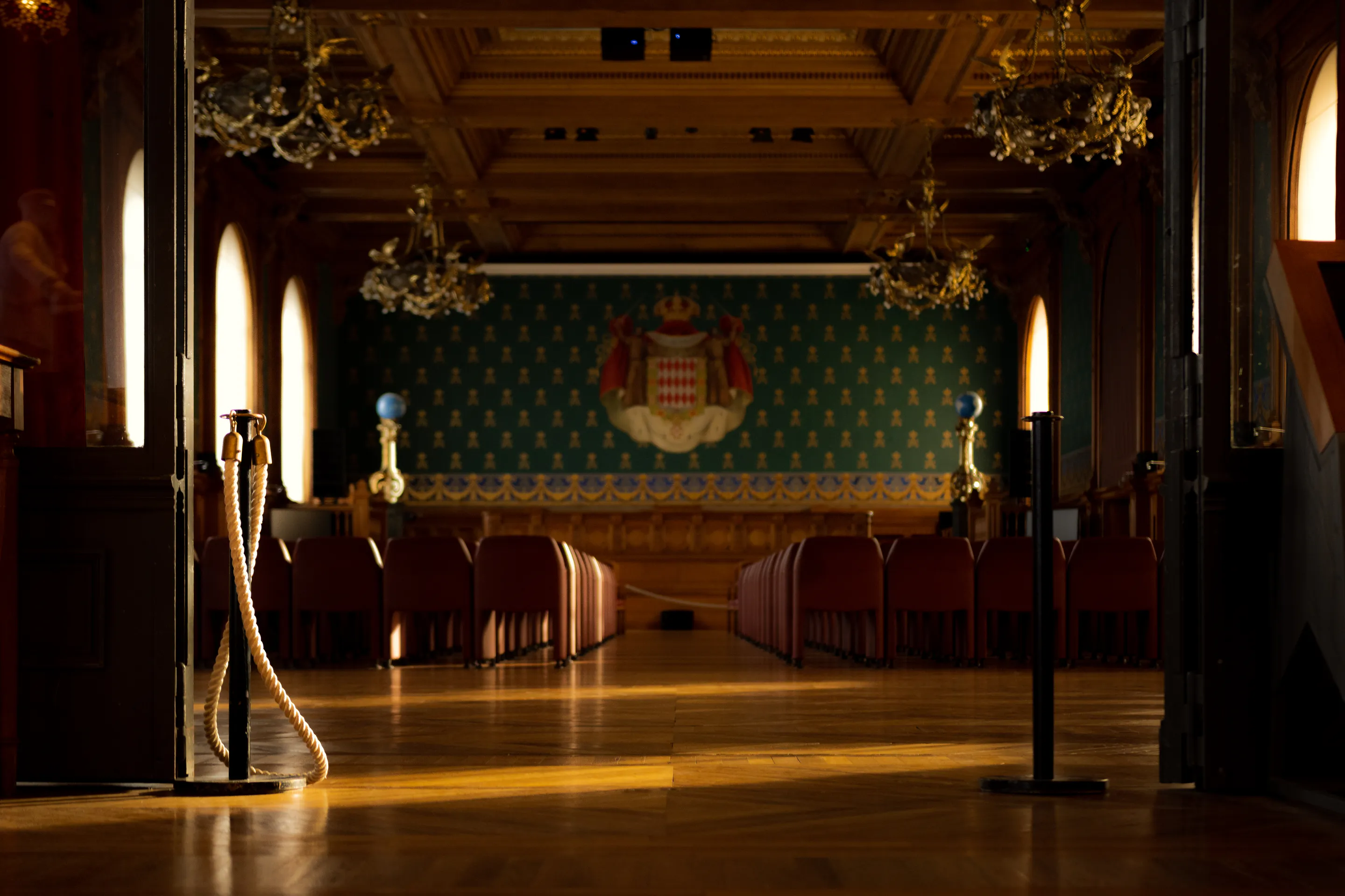 Wood-panelled ballroom — chandeliers, tapestry, red chairs on sunlit parquet