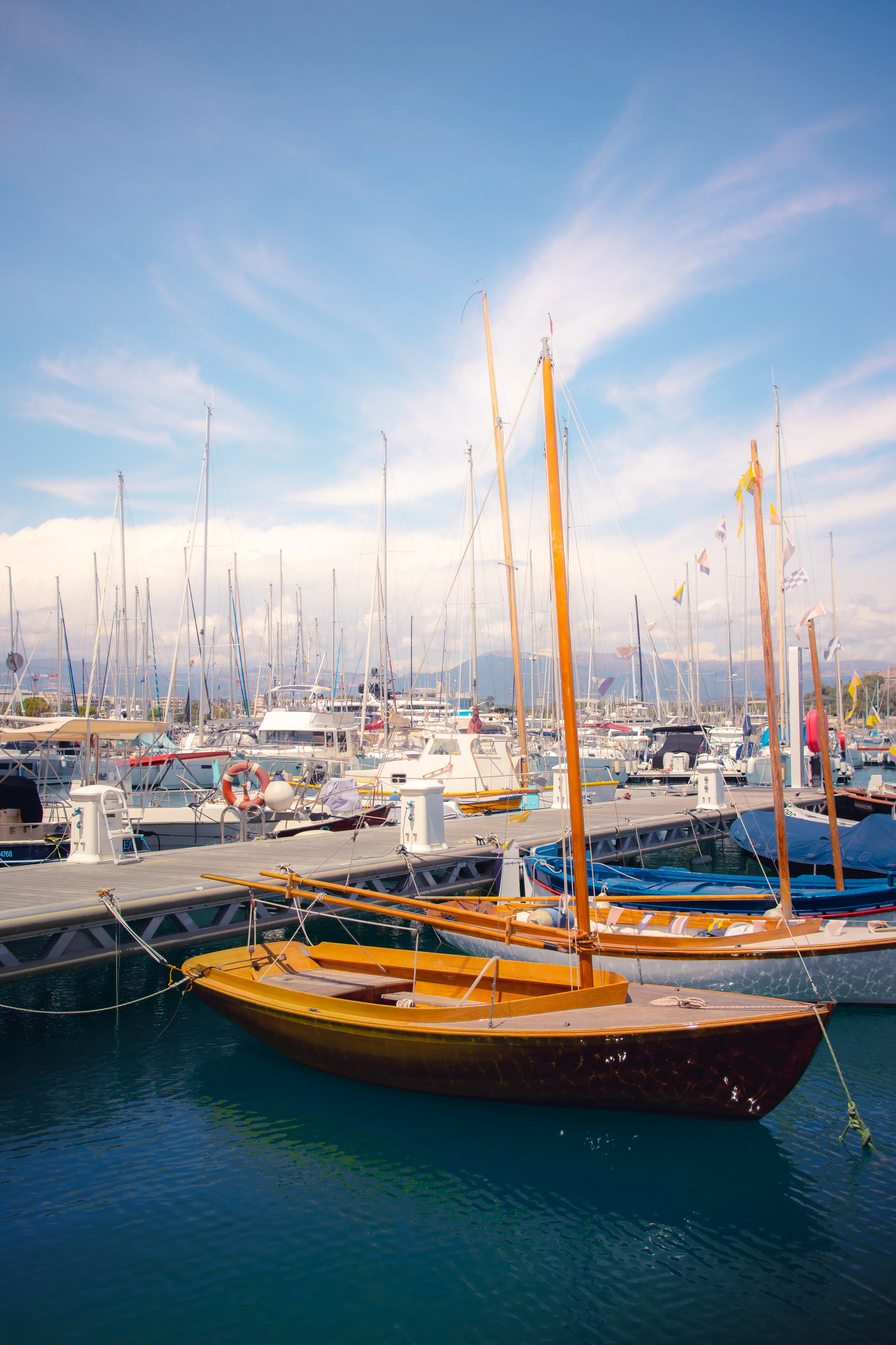 Varnished wooden sailboat moored among the plastic hulls