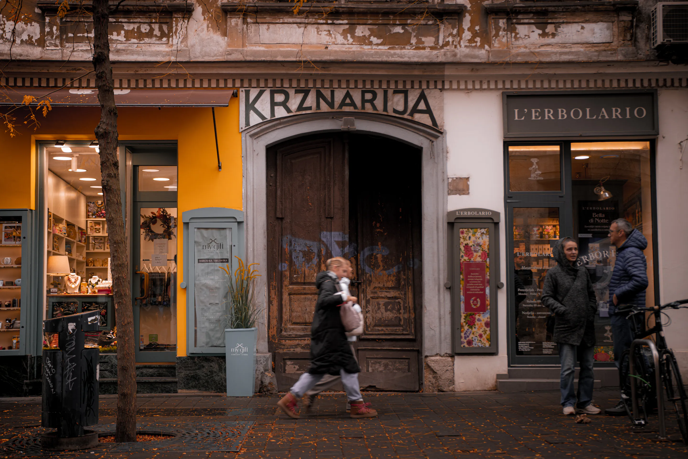 A passer-by blurred across the mustard KRZNARIJA shopfront